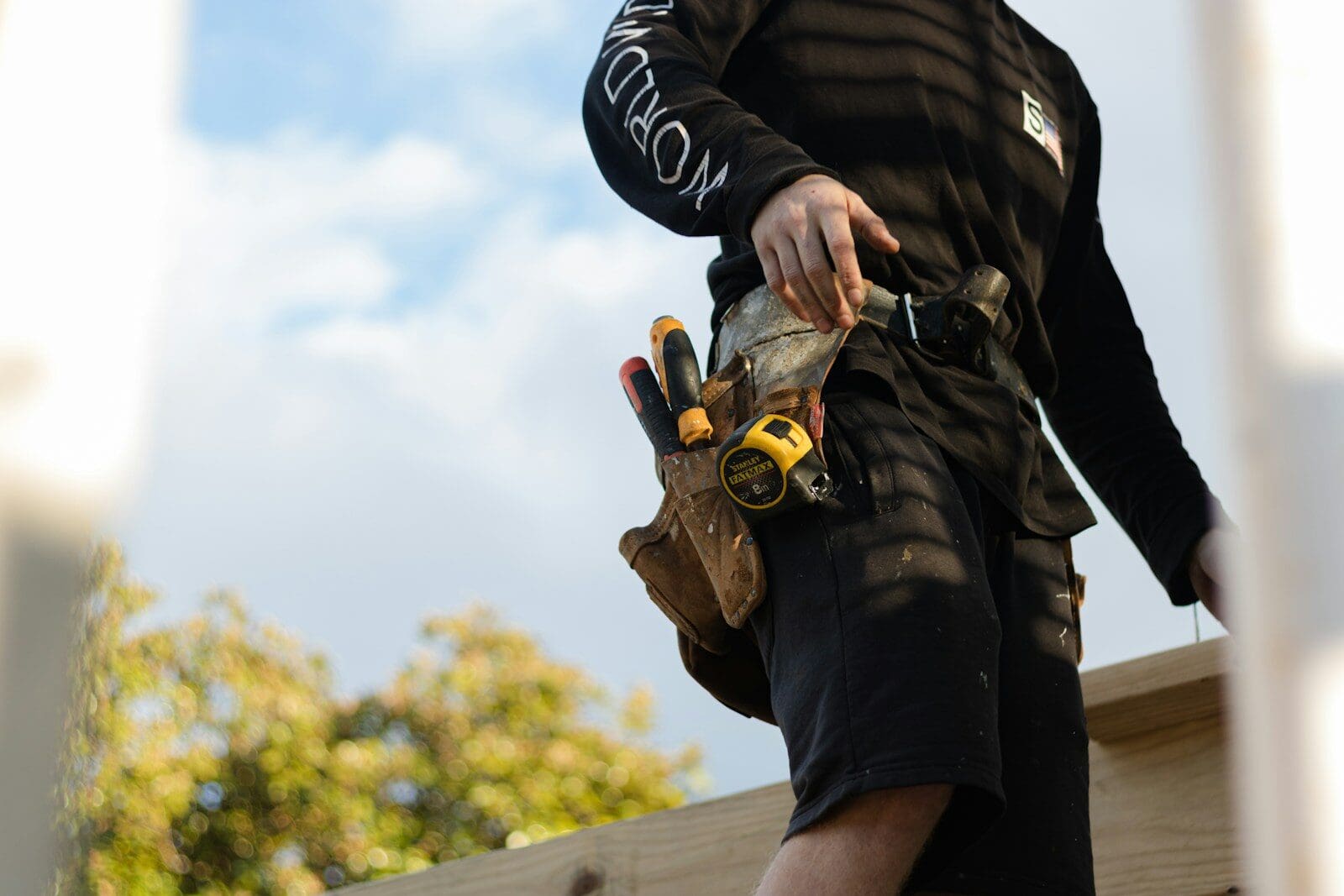 A person in a black long-sleeved shirt wearing a leather tool belt with tape measure